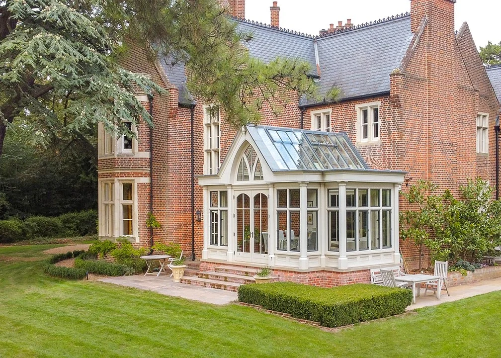 Bespoke conservatory with Gothic arched glazing and pitched glass roof adjoining a traditional red brick country house